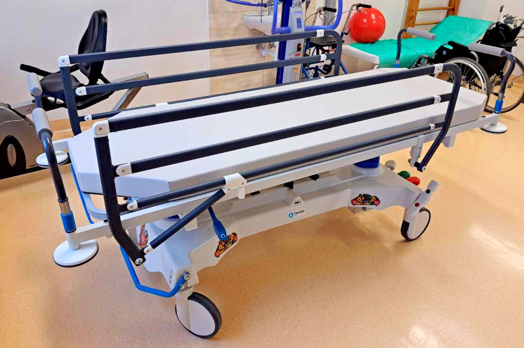 Zdjęcie przedstawia nowoczesny wózek do przewożenia pacjentów.